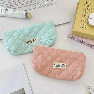 Détail de trousses de maquillage matelassées vert menthe et pêche avec étiquettes tissées