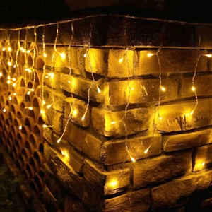 Warm yellow LED icicle curtain lights hanging on a vintage brick wall for festive decor
