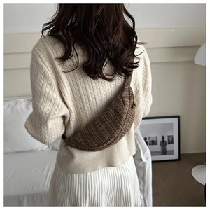 Rear view of a textured brown striped crossbody bag on a model in a cozy setting
