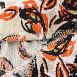 Makroaufnahme von geblümtem Plissee-Stoff mit orange-schwarzen Mustern und Overlock-Naht