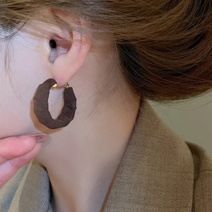Detail of dark brown hoop earrings with spiral pleated texture on a model wearing brown coat