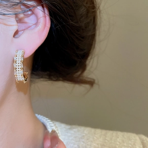 Close-up of C-shaped gold-plated earring with pearls and cubic zirconia on model