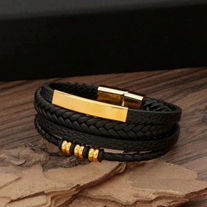 Close-up of black braided leather bracelet with golden metal accents on bark background