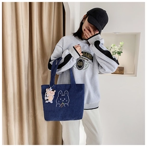 Detail of dark blue corduroy tote bag with rabbit embroidery and cow plush charm