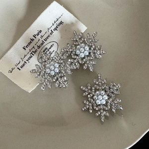 Macro detail of silver snowflake earrings with sparkling rhinestones and center pearls