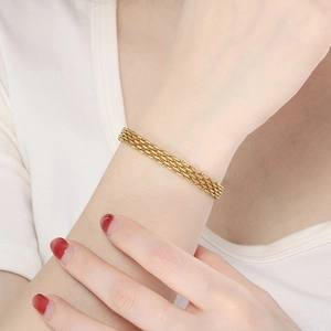 Close-up of a layered gold titanium steel braided bracelet on a female wrist model