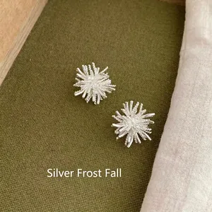 Detail of silver flower stud earrings with a sparkling matte finish and starburst design
