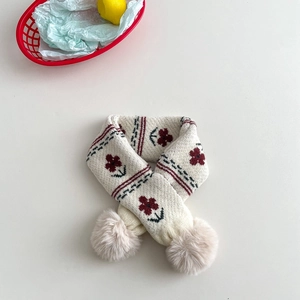 Close-up of knit kids scarf with red flower patterns and beige pom-poms on white background