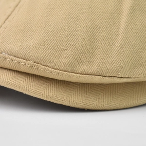 Close-up of beige herringbone fabric and fine stitching on a vintage newsboy cap