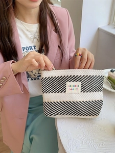 Striped woven makeup bag with large capacity and logo patch held by a model in a cafe