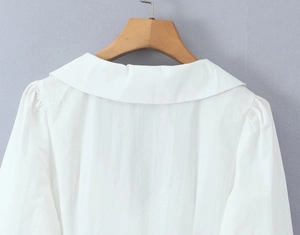 Detail of the white cotton blouse rear collar and shoulder seams on a wooden hanger