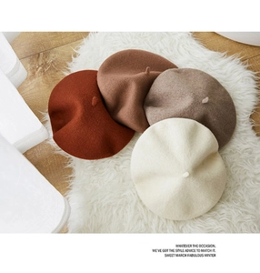 Flat lay of wool beret hats in red-brown, dark brown, and beige on a white plush rug