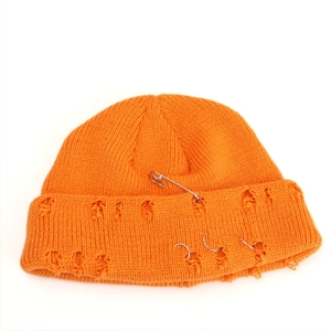 Close-up of orange knitted beanie with distressed holes, metal rings, and silver pin details