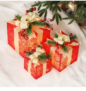Close-up of three lighted red plaid Christmas gift boxes with pine cones and golden bows