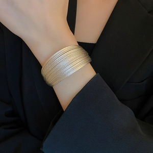 Detail shot of multi-layered gold wide cuff bracelet on wrist against black suit
