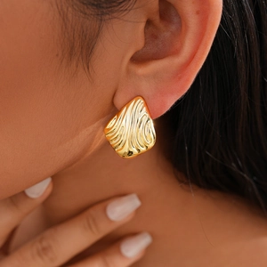 Close-up of golden irregular textured teardrop earring worn by a model