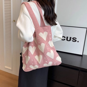 Close-up of pink knitted tote bag with white heart patterns and wide shoulder strap