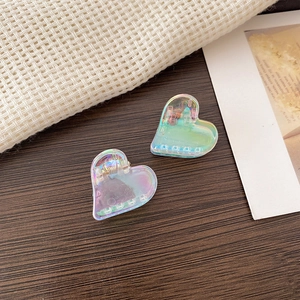 Detail of colorful laser heart-shaped hair claws with iridescent finish on wooden surface