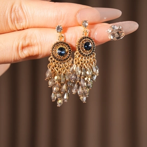 Close-up of Bohemian gold earrings with dark blue glass stones and grey crystal tassels