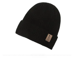 Close-up of black ribbed knit beanie with brown leather brand tag and folded cuff detail
