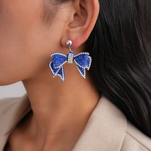 Close-up of elegant blue bow earrings with sparkling pavé crystals worn by a model