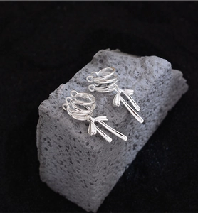 Detail of silver ribbon bow ear cuffs placed on a textured grey stone backdrop