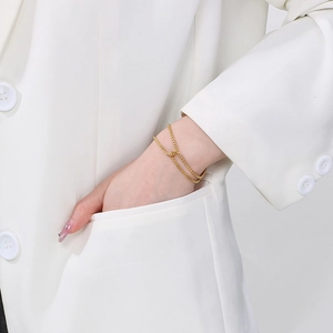 Close-up of a layered gold stainless steel chain bracelet worn by a model in a white suit