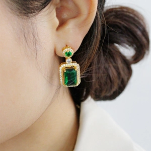 Elegant gold earrings with emerald green rectangle stone and zircon halo on model