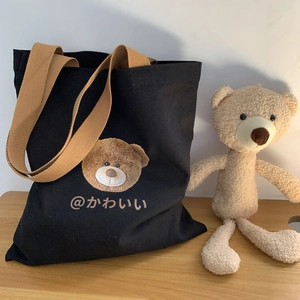Detail of a black canvas tote bag featuring a cute teddy bear print and brown fabric strap