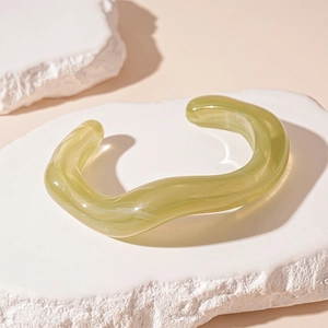 Detailed view of green wavy acrylic open bangle with marble texture on white stone boards