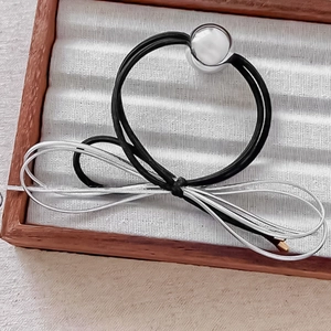 Close-up of multi-strand elastic hair tie with polished silver metal bead on wooden tray