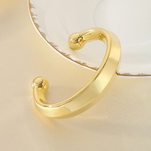 Gros plan d'un bracelet jonc doré en C avec perles aux extrémités sur porcelaine