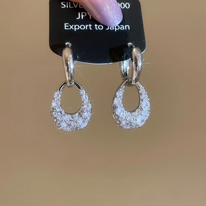 Macro detail of silver C-shape drop earrings with sparkling cubic zirconia on display card
