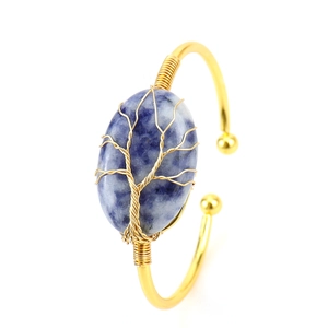 Detail of tree of life wire-wrapped gold bracelet with oval blue stone on white background