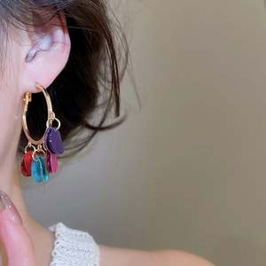 Close-up of model wearing gold hoop earrings with multi-colored teardrop pendants