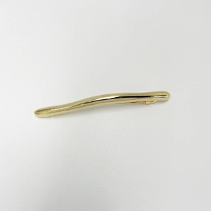 Detail shot of wavy gold-toned metal hair clip featuring a glossy finish and minimalist design