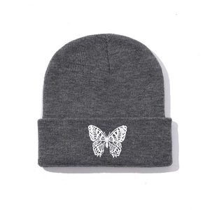 Close-up of white butterfly embroidery on a grey ribbed knit beanie with folded cuff
