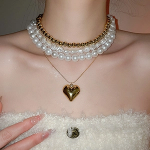 Détail de colliers de perles superposés avec pendentif cœur doré sur un pull blanc doux