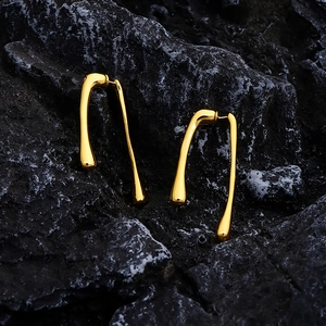 Detail of long gold drop earrings with a fluid organic design on a dark rock background