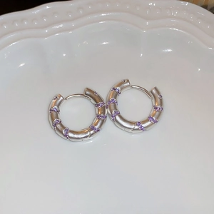 Detail of silver hoop earrings with spiral purple zircon inlay on a white ceramic tray