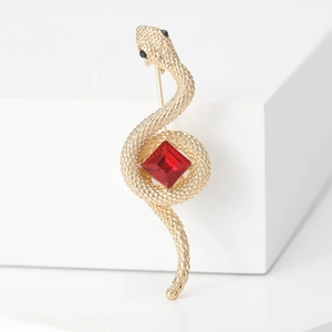 Vintage golden cobra brooch with red square gemstone and scaly texture on white background