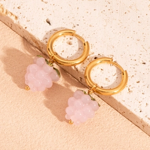 Détail de créoles dorées avec pendentifs de raisin rose sur une surface en pierre
