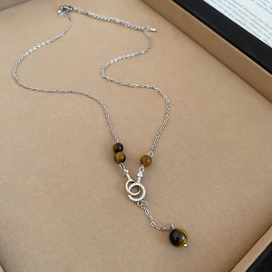 Macro detail of silver necklace with tiger eye beads and pavé gender symbol pendant