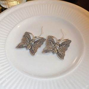 Detail of vintage silver butterfly drop earrings with intricate textured wings on ceramic