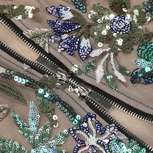 Detail of floral embroidery with multicolored sequins and metal zipper on mesh fabric