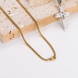 Gold box chain necklace with a silver cross pendant displayed on a textured stone