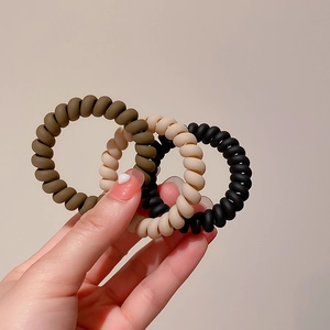 Three-piece matte spiral hair ties set in earthy tones held by hand for scale