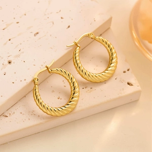 Détail macro de boucles d'oreilles créoles torsadées dorées sur une surface en pierre