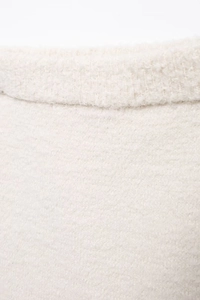 Close-up of cream knit fabric texture with fringe detailing on elegant cardigan set