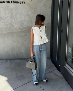 Outdoor shot of sleeveless white pleated top with tie neckline and light blue jeans